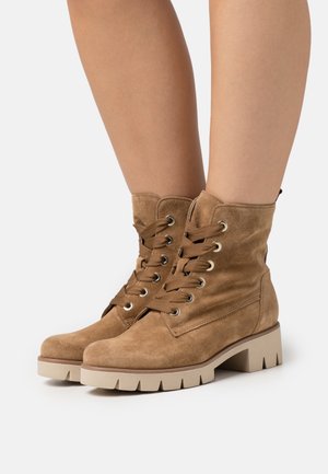 Brown suede ankle boots with a round toe, lace-up front, and rubber sole. Features metal eyelets and a textured finish.