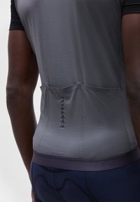 Bakhode av en person som har på seg en tettsittende grå sykkeltrøye med tre baklommer og Castelli-logo, kombinert med marineblå polstrede sykkelshorts.