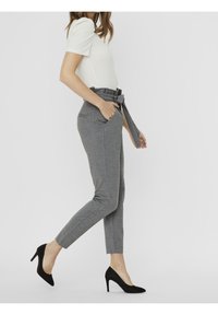 Grå smal passform byxor med hög midja, knytbälte och sidfickor, ihopparade med svarta spetsiga klackar och en åtsittande vit topp.