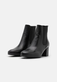 Bottes noires à cheville en cuir lisse, avec des panneaux latéraux élastiques, un bout arrondi et un talon bloc. Design simple sans ornements.