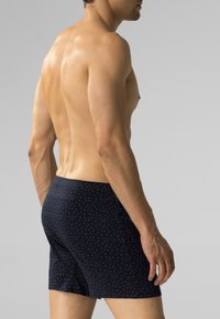 Granatowe bokserki w wzory z małymi białymi kropkami. Miękka tkanina, elastyczny pas i dopasowany krój. Model widziany z boku.