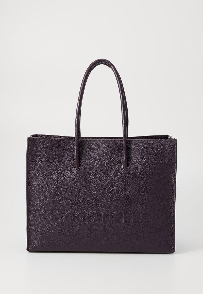 Purple leather tote bag with two long handles, embossed logo on the front, and a textured surface. Closed top with a zipper.