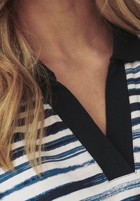 Polo avec un col bleu marine, présentant des rayures horizontales bleues et blanches. Le tissu semble doux avec un léger éclat.