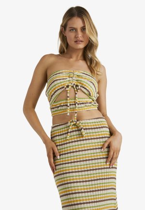 Donna che indossa un completo a due pezzi lavorato a maglia a righe con colori giallo, verde, marrone e bianco, caratterizzato da un top senza spalline con un fiocco frontale e una gonna coordinata.