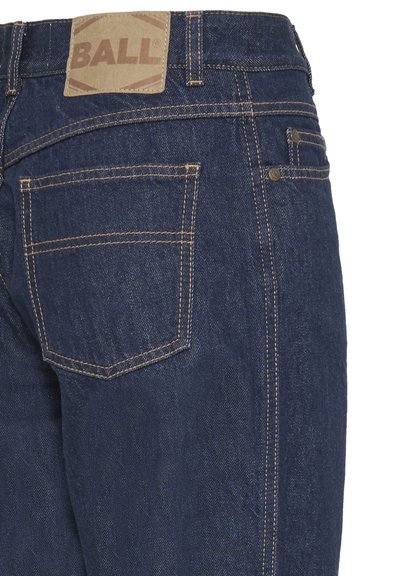 Jean en denim bleu foncé avec une étiquette en cuir brun portant l'inscription "BALL." Présente des coutures orange, un design à cinq poches et une coupe légèrement ajustée.