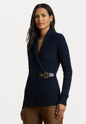 Marinblå stickad cardigan med kabelmönster, sjalkrage och bälte i midjan, med bruna bältesdetaljer och ribbade ärmslut.