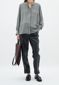 Blusa di seta grigia con colletto alla cinese e chiusura con bottoni, abbinata a pantaloni di pelle nera e una borsa a tracolla marrone, completata da mocassini neri.