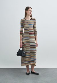 Ριγέ πλεκτό φόρεμα με μακριά μανίκια, με οριζόντιες γραμμές σε απαλούς τόνους. Συνδυασμένο με μαύρη τσάντα και φλατ παπούτσια.