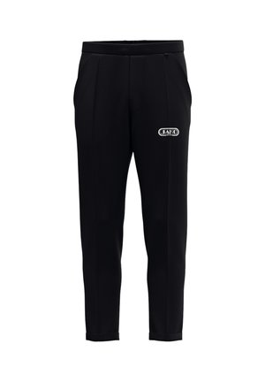 Pantalones negros ajustados con bolsillos laterales y un pequeño logo blanco de JAKO Sport en el muslo derecho, con una cintura ajustada y bajos remangados.