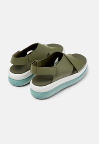 Olive green sandals with cross straps and adjustable velcro closure. Features a rounded, white sole with a light blue accent.