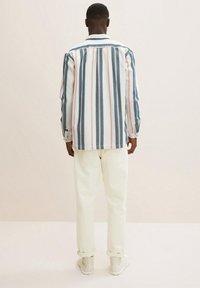 Pasiasta koszula w kolorach białym, niebieskim i różowym; luźny krój z kołnierzykiem i mankietami. Połączona z kremowymi spodniami i białymi sneakersami. Widok z tyłu.