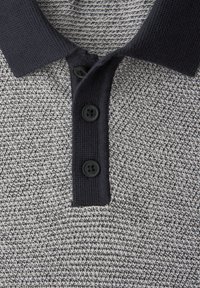 Polo à texture grise et blanche avec un col bleu marine, doté de trois boutons noirs et d'un motif en tissu tricoté.