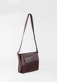 Brown leather messenger bag with a long shoulder strap, zippered front pocket, and flat base, featuring smooth texture and minimal stitching.