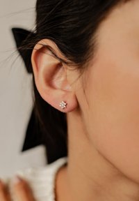 Pendientes de plata con un diseño floral que incluye piedras claras y brillantes. El pendiente está posicionado cerca de la oreja, mostrando detalles delicados.