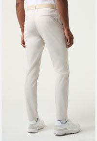 Jasnobeżowe spodnie wykonane z gładkiej tkaniny, z talią ozdobioną brązowym paskiem, tylnymi kieszeniami i zwężanymi nogawkami. Noszone z białymi trampkami.