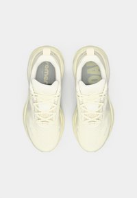 Scarpe da corsa color crema con tomaia in rete, suola testurizzata e lacci leggeri. Presentano un logo sottile sulla linguetta e un collarino imbottito.