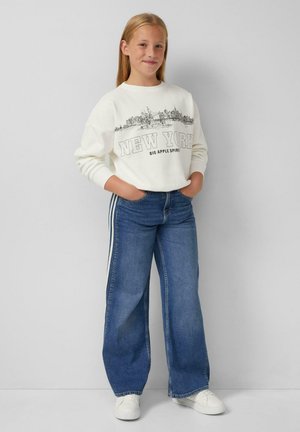 Witte sweatshirt met "NEW YORK" in zwart gedrukt, gecombineerd met brede spijkerbroek in het blauw met zijstrepen, en witte sneakers.