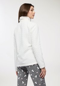 Biała polarowa kurtka z teksturowanym wzorem chevron, z wysokim kołnierzem. Połączona z szarymi legginsami ozdobionymi motywami pingwinów i serc.