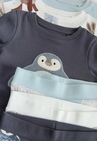 Dark gray sweatshirt featuring a penguin appliqué on the front, with light blue, white, and patterned shirts layered underneath.