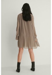 Abito corto a pois con maniche lunghe, realizzato in tessuto trasparente, con gonna arricciata. Indossato con stivaletti neri alla caviglia.