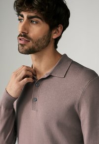 Licht mauve lange mouwen polo shirt met geribde kraag, drie donkere knopen en een zachte textuur. Strak design met subtiele stiksels.