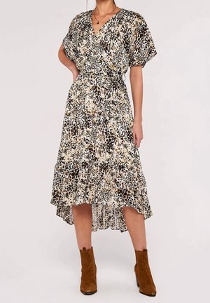 Kobieta ubrana w beżowo-brązową sukienkę kopertową w panterkę z falbanami na rękawach oraz brązowe zamszowe botki za kostkę.