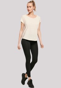 Light cream short-sleeve t-shirt with a scooped neckline, paired with black fitted leggings and black athletic shoes.