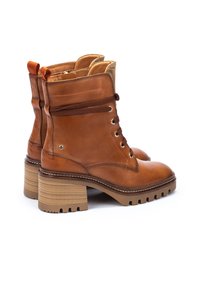 Botas de tobillo de cuero marrón con un acabado texturizado, parte superior con cordones y un tacón grueso y estriado. Presenta tiradores en contraste naranja.