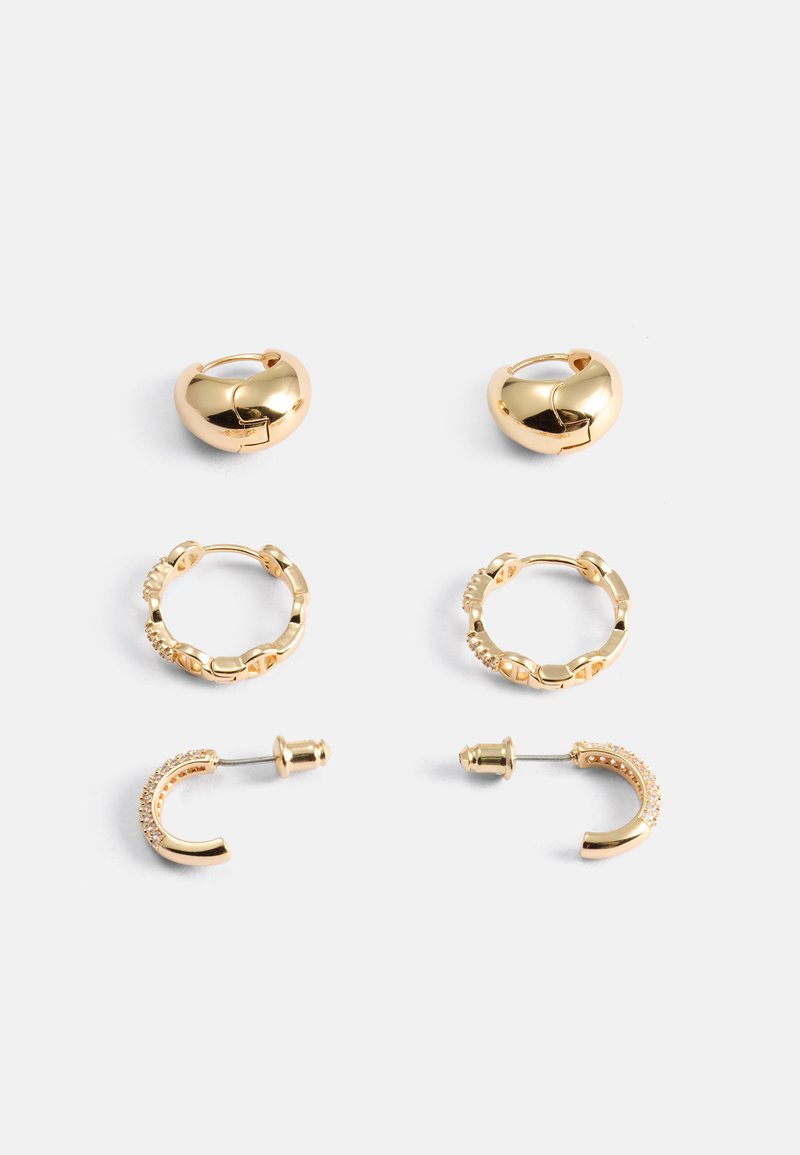 Zlaté kruhové náušnice ve tvaru srdce, s texturovanými články a zakřiveným designem, jedna dvojice obsahuje malé krystaly, celkem čtyři odlišné styly.