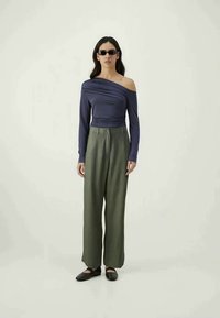 Navy off-shoulder top with gathered texture, paired with high-waisted, wide-leg olive green trousers and black slip-on shoes.