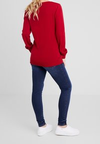 Red knitted sweater with long sleeves, ribbed cuffs and hem, paired with dark blue skinny jeans and white sneakers.