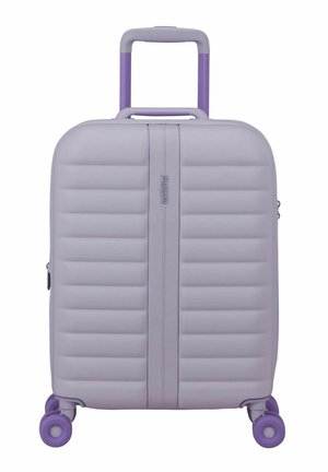 Valise rigide lavande avec des rainures horizontales, poignée rétractable et quatre roues pivotantes violettes, vue de face.