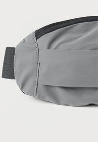 Γκρι τσάντα ζώνης από ύφασμα με κομψό σχέδιο, διαθέτει ομαλή υφή, μαύρες λεπτομέρειες και ρυθμιζόμενο λουράκι για ασφαλή εφαρμογή.