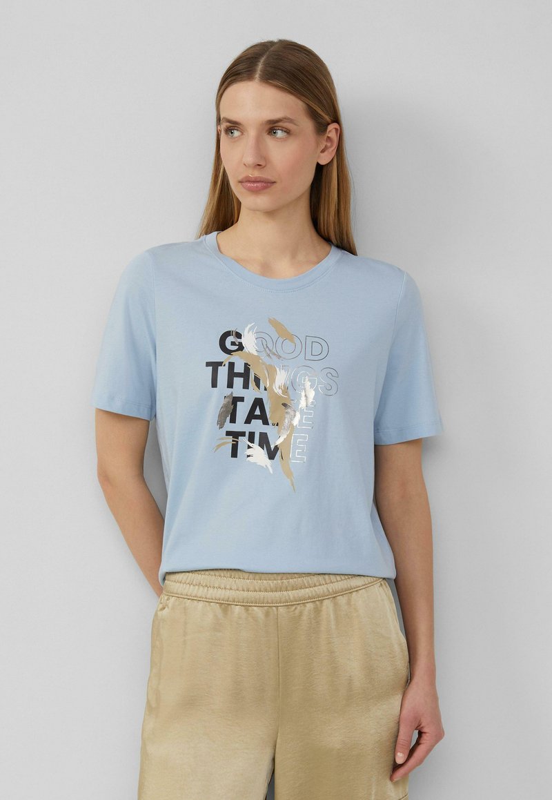 Lichtblauw katoenen T-shirt met korte mouwen, voorzien van een grafische print in zwart en metallic goud, waarop de tekst "GOEDE DINGEN HEBBEN TIJD NODIG." staat.