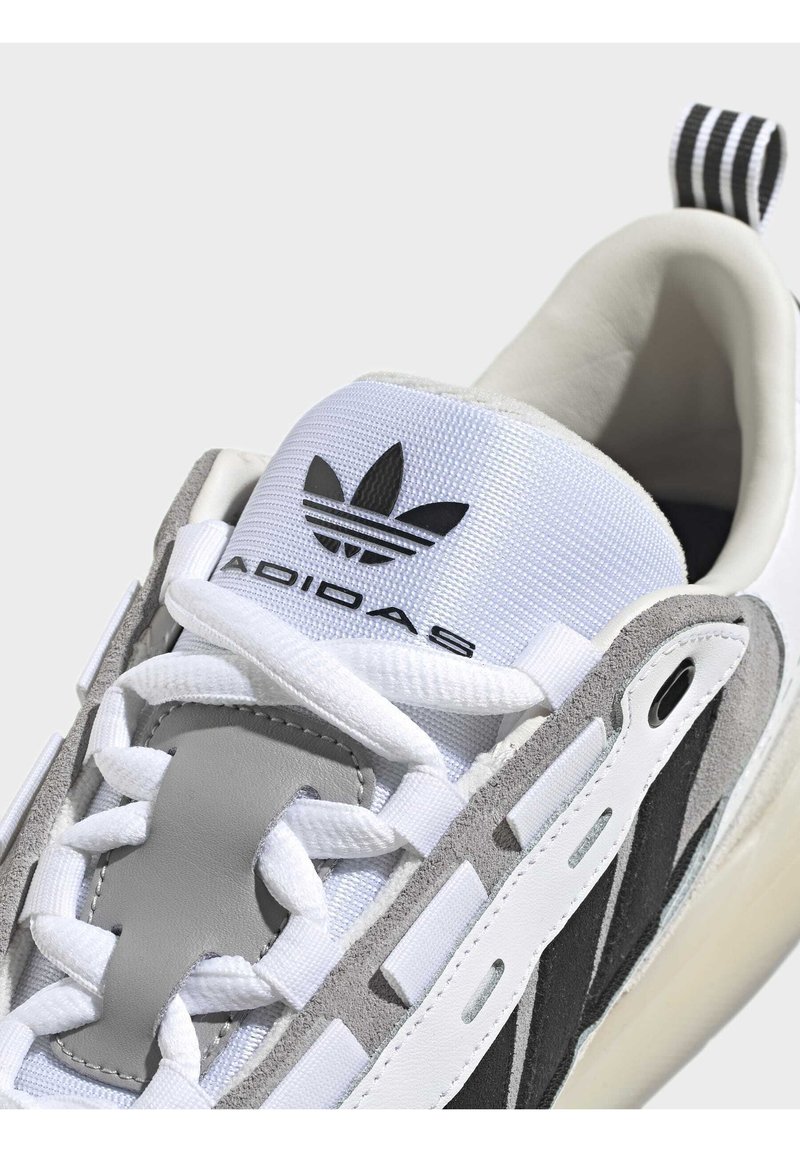 Białe i szare sneakersy sportowe z chropowatą siateczką, zamszowymi akcentami, czarnym logo oraz unikalnie ukształtowaną podeszwą.