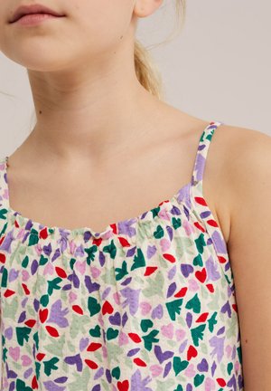 Mlada osoba nosi majicu bez rukava s višebojnim uzorcima srca i listova u zelenoj, crvenoj, ljubičastoj i ružičastoj boji na bijeloj pozadini.