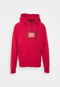 Sudadera roja con capucha que presenta un bolsillo frontal, cordones en la capucha y texto del logo en negro. Fabricada con un material suave y con puños y dobladillo acanalados.