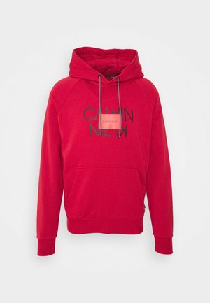 Sweat à capuche rouge avec une poche avant, un capuchon à cordon de serrage et un texte en logo noir. Fabriqué en matériau doux avec des poignets et un ourlet côtelés.