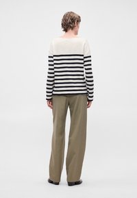 Ριγέ μπλούζα μακρυμάνικη σε κρέμα και μαύρο, με άνετη εφαρμογή, συνδυασμένη με φαρδιά ελαιοπράσινα παντελόνια, λεία υφή και απαλή σχεδίαση.