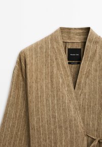 Vêtement de style kimono rayé marron, fabriqué en tissu texturé. Il présente un design enveloppant avec un lien et une étiquette à l'intérieur.