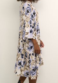 Robe florale aux tons bleus et beiges, avec une jupe à volants et des manches évasées. Fabriquée en tissu léger avec une texture douce.