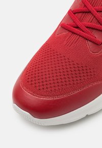 Scarpa sportiva rossa con tomaia in maglia testurizzata, accentuata da dettagli in pelle liscia e suola in gomma bianca, caratterizzata da punta arrotondata e chiusura con lacci.