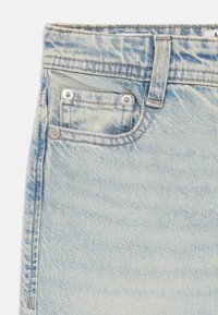 Light blue denim fabric with a textured surface, featuring a small front pocket with metal rivets and a belt loop above.