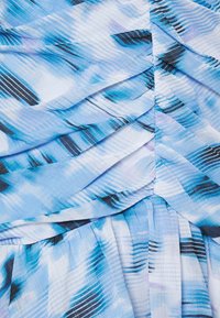 Modrá a bílá skládací látka s abstraktními černými a fialovými štětcovými vzory, vytvářející šikmé, překrývající se záhyby.