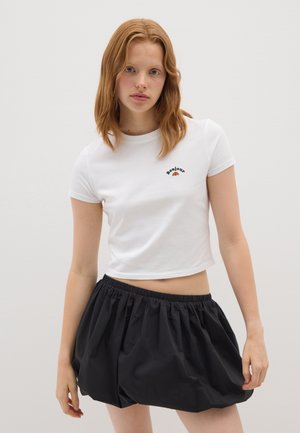 Camiseta blanca cortada con mangas cortas y bordado negro de "bonjour"; combinada con una falda negra con cintura elástica y fruncida.