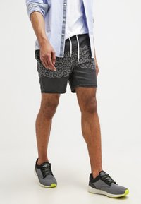 Black shorts with white floral pattern, drawstring waist, and contrasting panels. Paired with gray sneakers featuring neon accents.