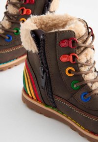 Stivaletti alla caviglia in tessuto marrone con rivestimento in pelliccia sintetica, occhietti colorati, zip laterale e strisce arcobaleno sul tallone. Suola in gomma per una buona aderenza.