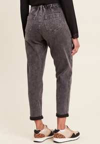 Grijs denim broek met een relaxte pasvorm, elastische tailleband, opgerolde manchetten en twee achterzakken, gecombineerd met beige en zwarte sneakers met een luipaardprint.