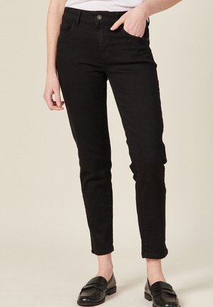 Zwarte, aansluitende jeans met een gladde textuur, vijf-pocket ontwerp en een knoopsluiting. Gecombineerd met zwarte instappers, wat zorgt voor een strakke silhouet.