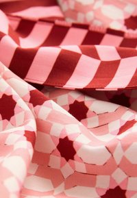 Audinys su rožiniais ir raudonais geometriniais raštais, žvaigždžių formomis, lygiu paviršiumi ir kontrastingomis juostelėmis įvairių atspalvių rožinės ir raudonos spalvos.